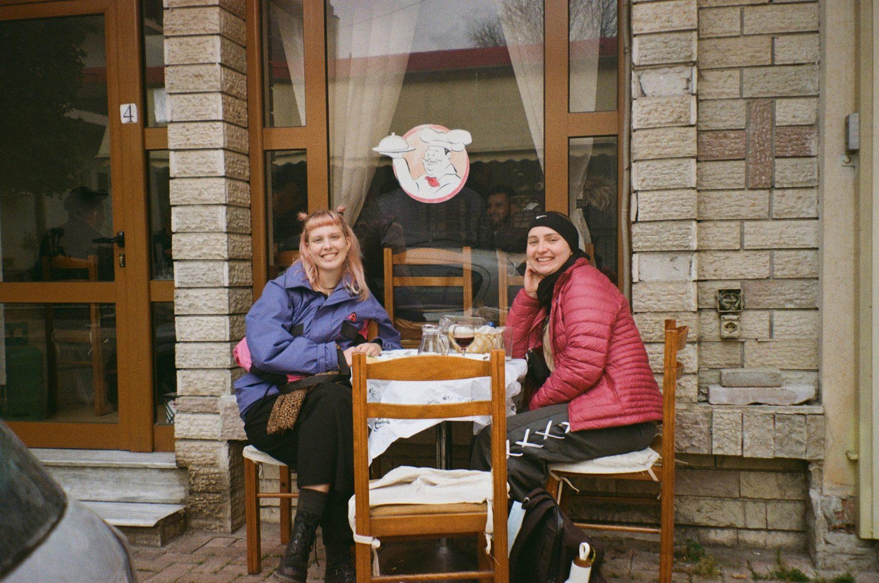 Dy shoqe qeshin në tavolinën e një kafeneje