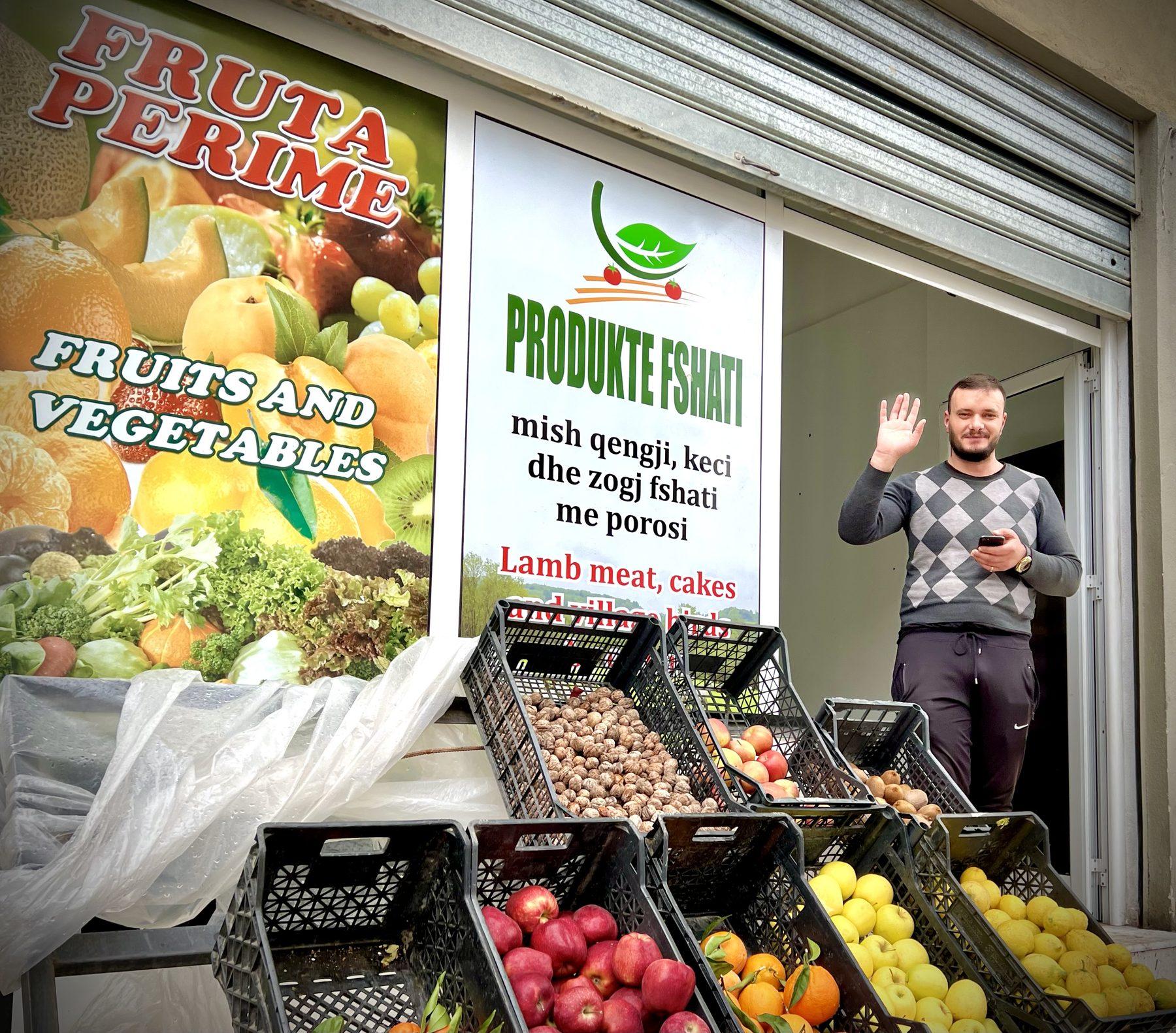 Një tregtar përshëndet para dyqanit me produkte fshati